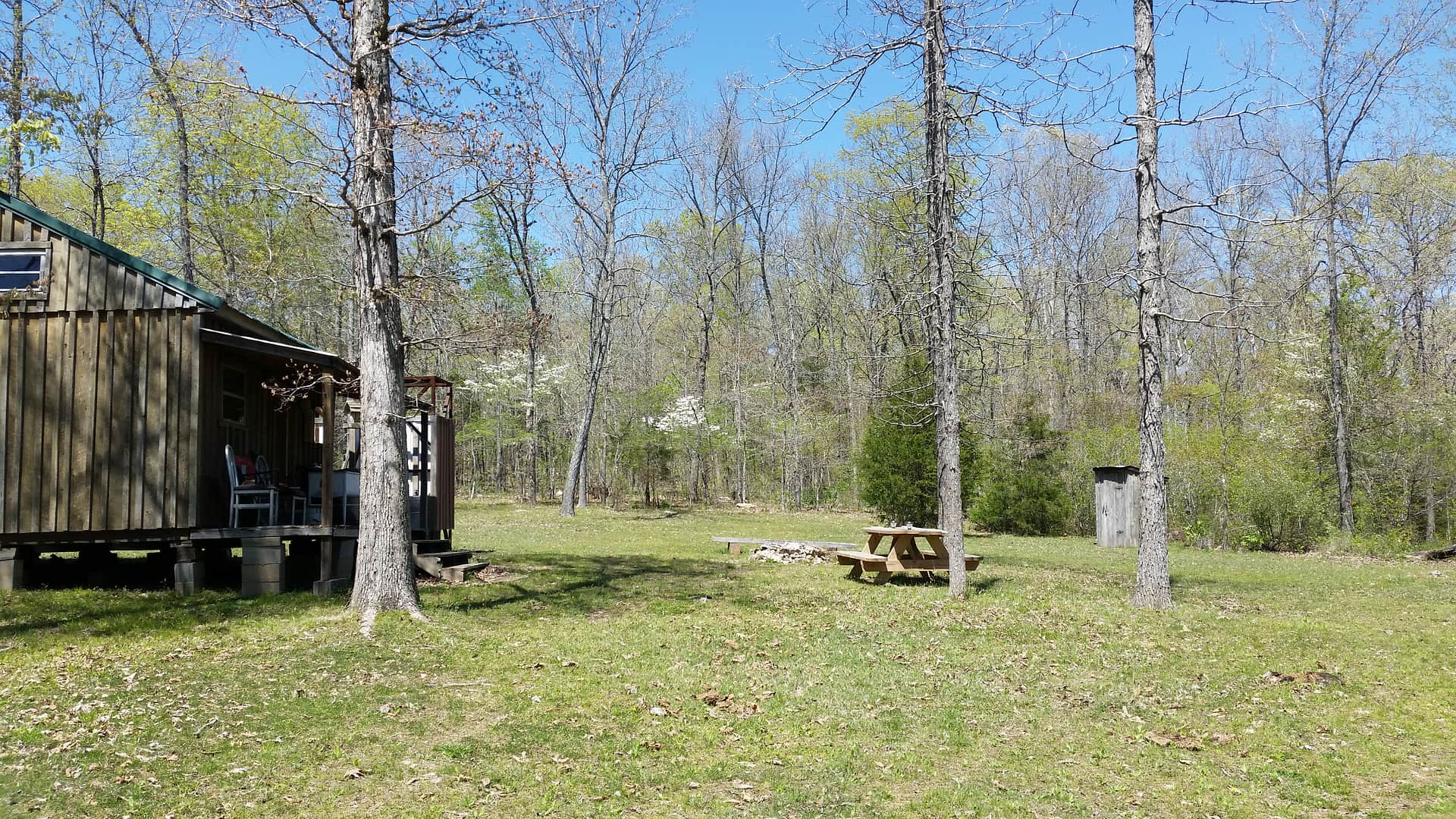Picnic and fire pit area off of the back porch. Outhouse for toileting at far right.