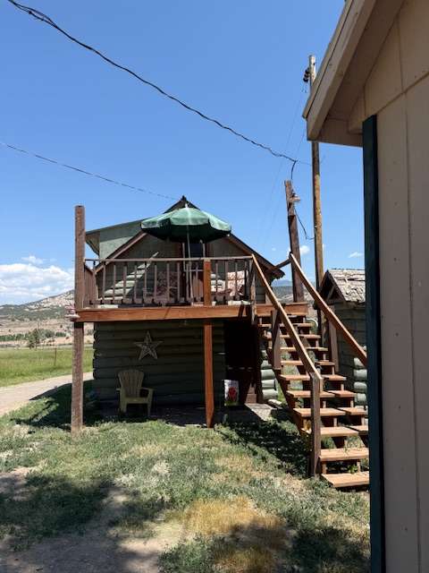 New sage green painted cabin,  adirondack chairs with cushions and shade umbrella up on deck