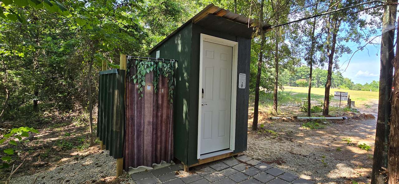 Toilet and sink with outdoor shower behind Site C. For use by sites A, B, and C with a code.