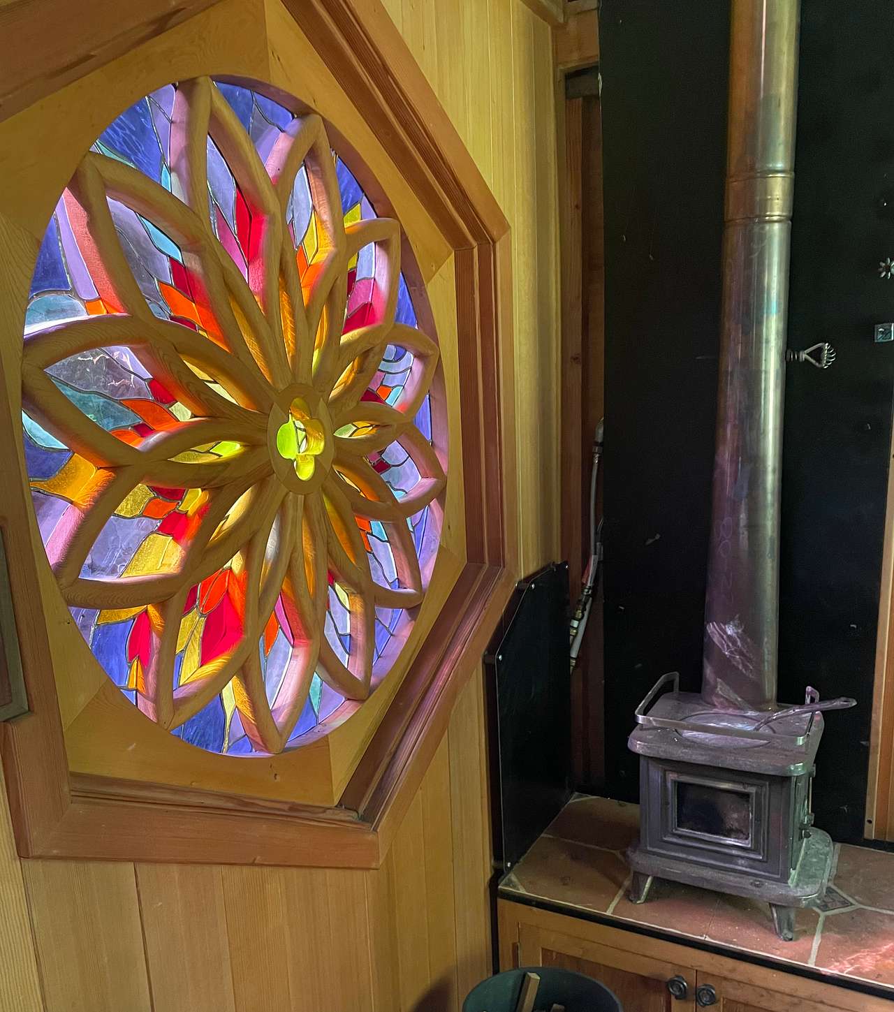 The inside of the cabin showing the tiny wood stove and the stained glass window.
