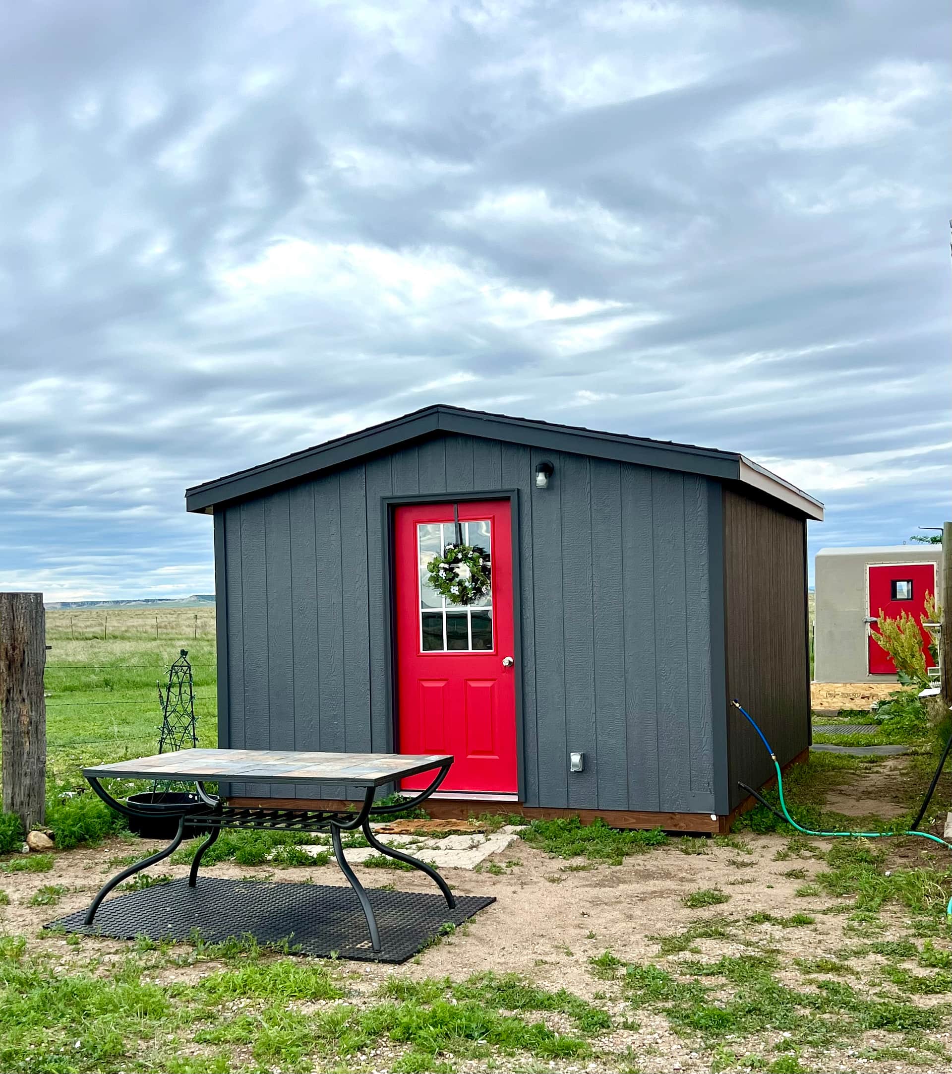 BADLANDS BUNKHOUSE Prairie Retreat, a cozy 12’ x 14’ insulated cabin with a tiny kitchen, stovetop, fridge, sink, basic kitchen supplies, TV, AC and heat. The BADLANDS BATHHOUSE in the background is also part of your private site, and has a compost toilet and hot/cold shower.