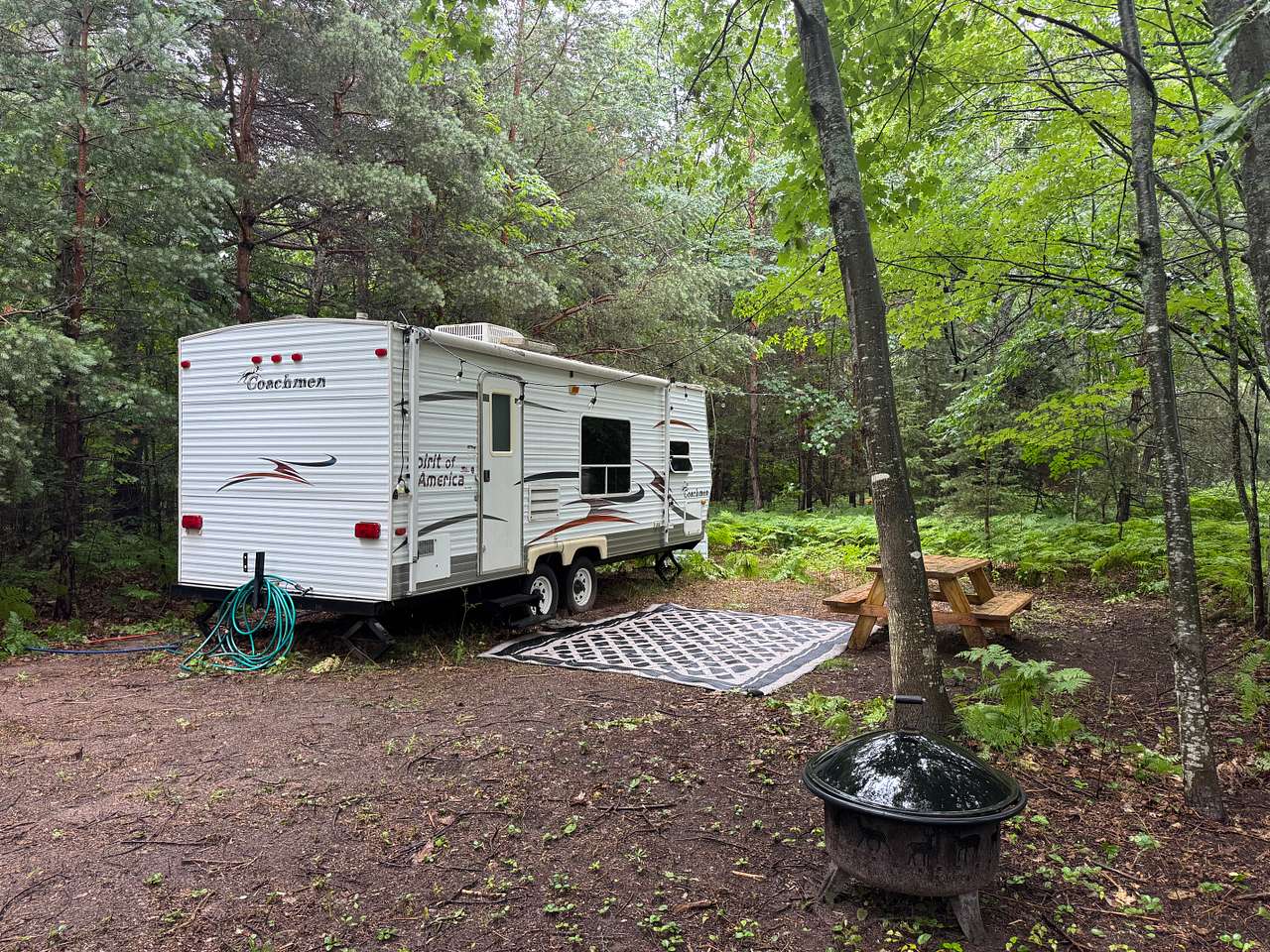 Camper and site with picnic table outdoor carpet lights, outdoor hose and fire pit.