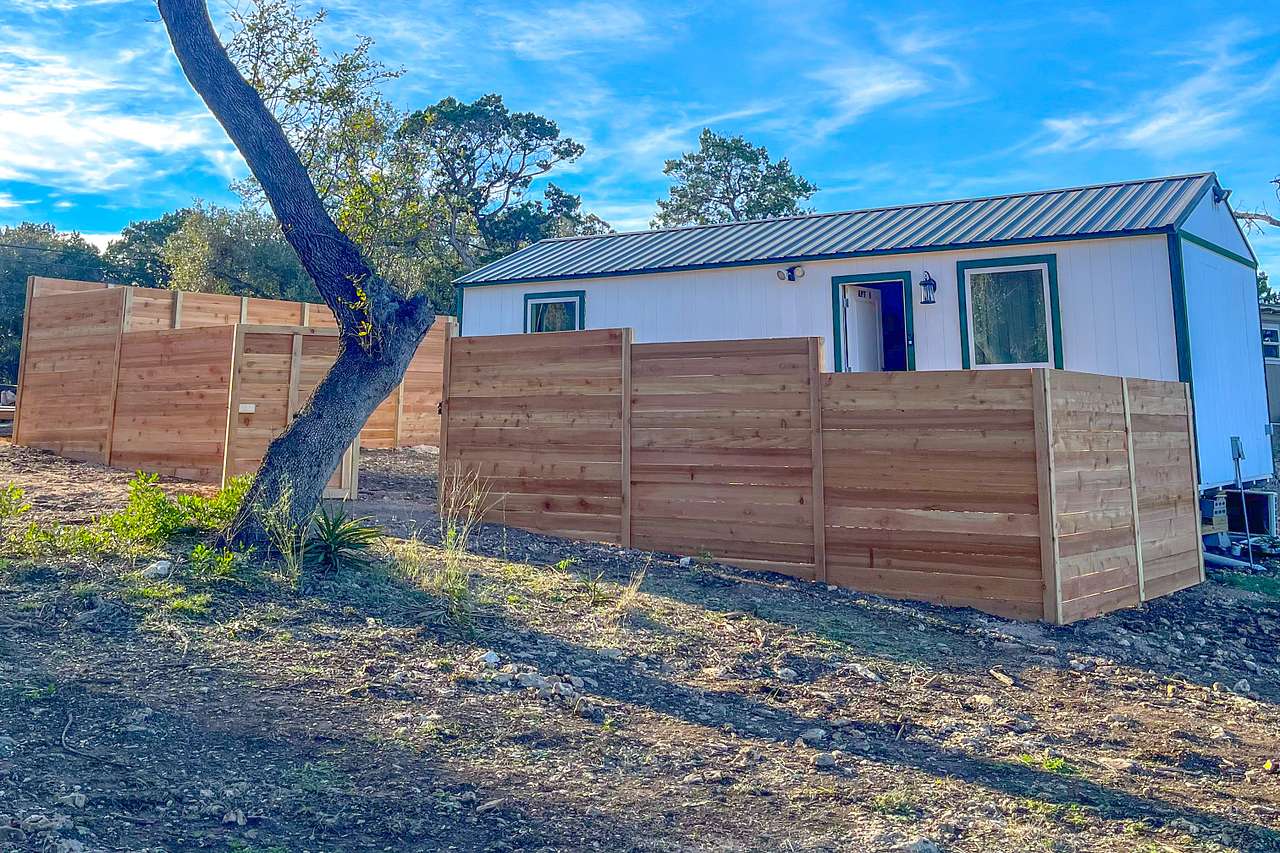 White Casita exterior and cedar-fenced yard in Lakehills, Texas.