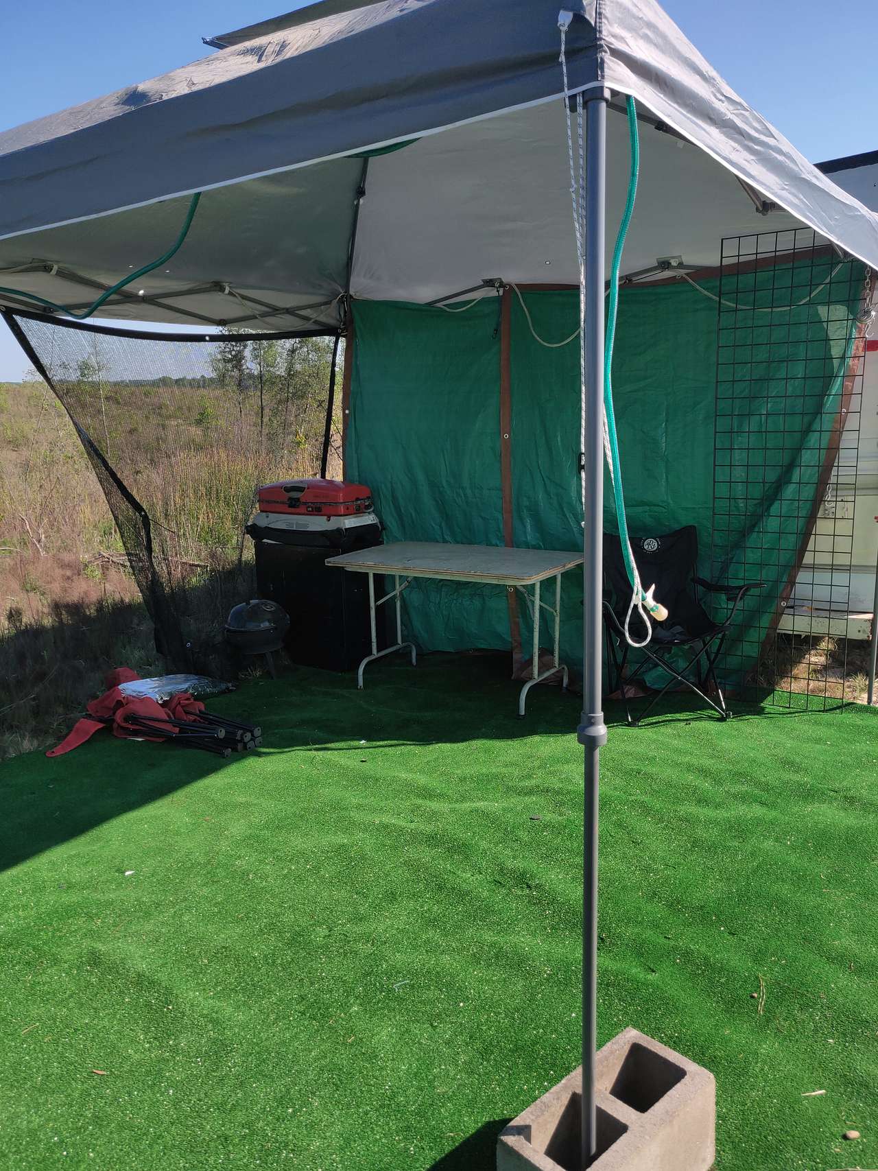 Outdoor lounge and cooking area with small charcoal and gas grill, chairs, table, canopy, and outdoor carpet