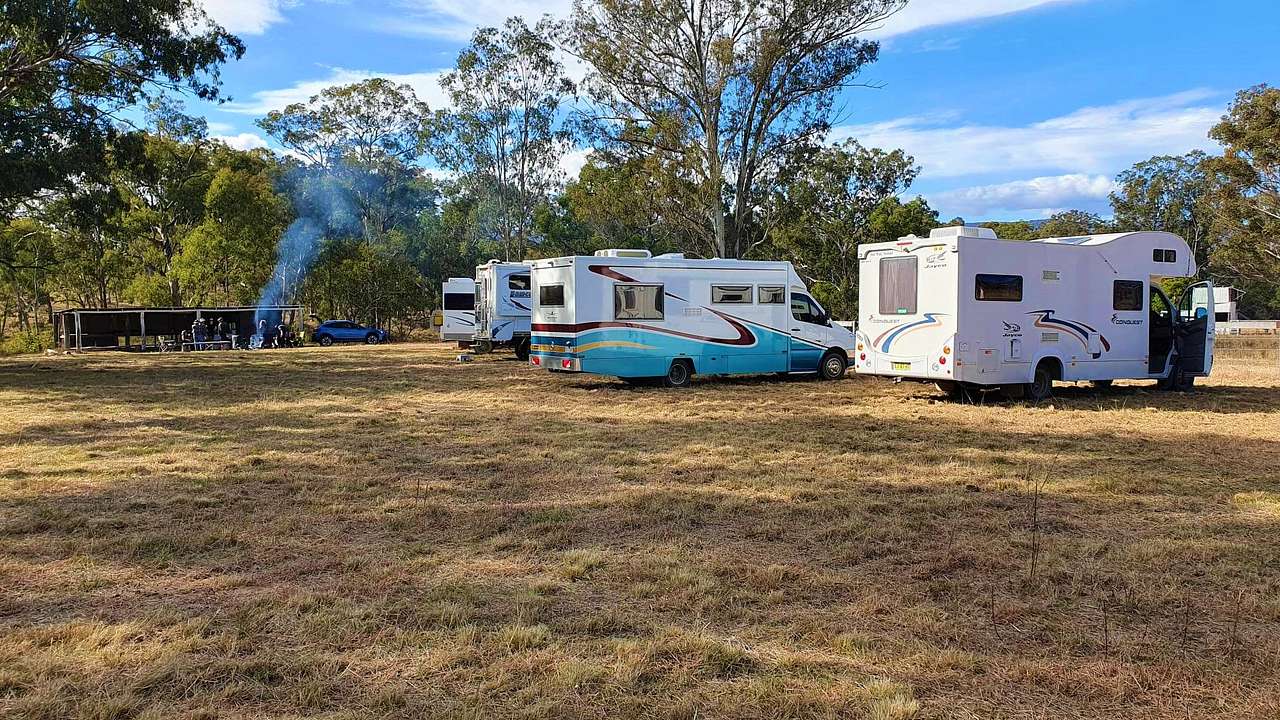 The Grounds campsite is 1.5 acres of level mowed grass. Motorhomes in foreground. Rustic Bar with fire going in background.