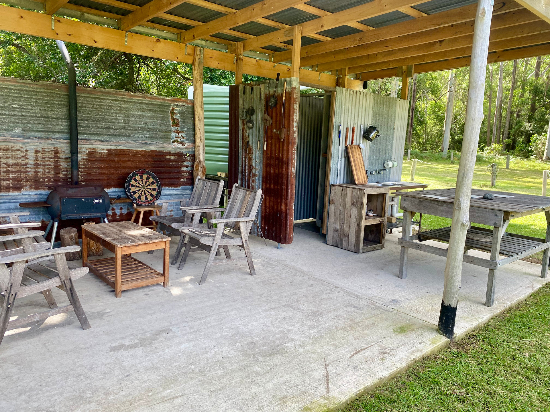 Inside shot of covered camping area including Oz Pig Big Pig, wooden camping furniture, sink, shower and rain water tank to the rear of the site