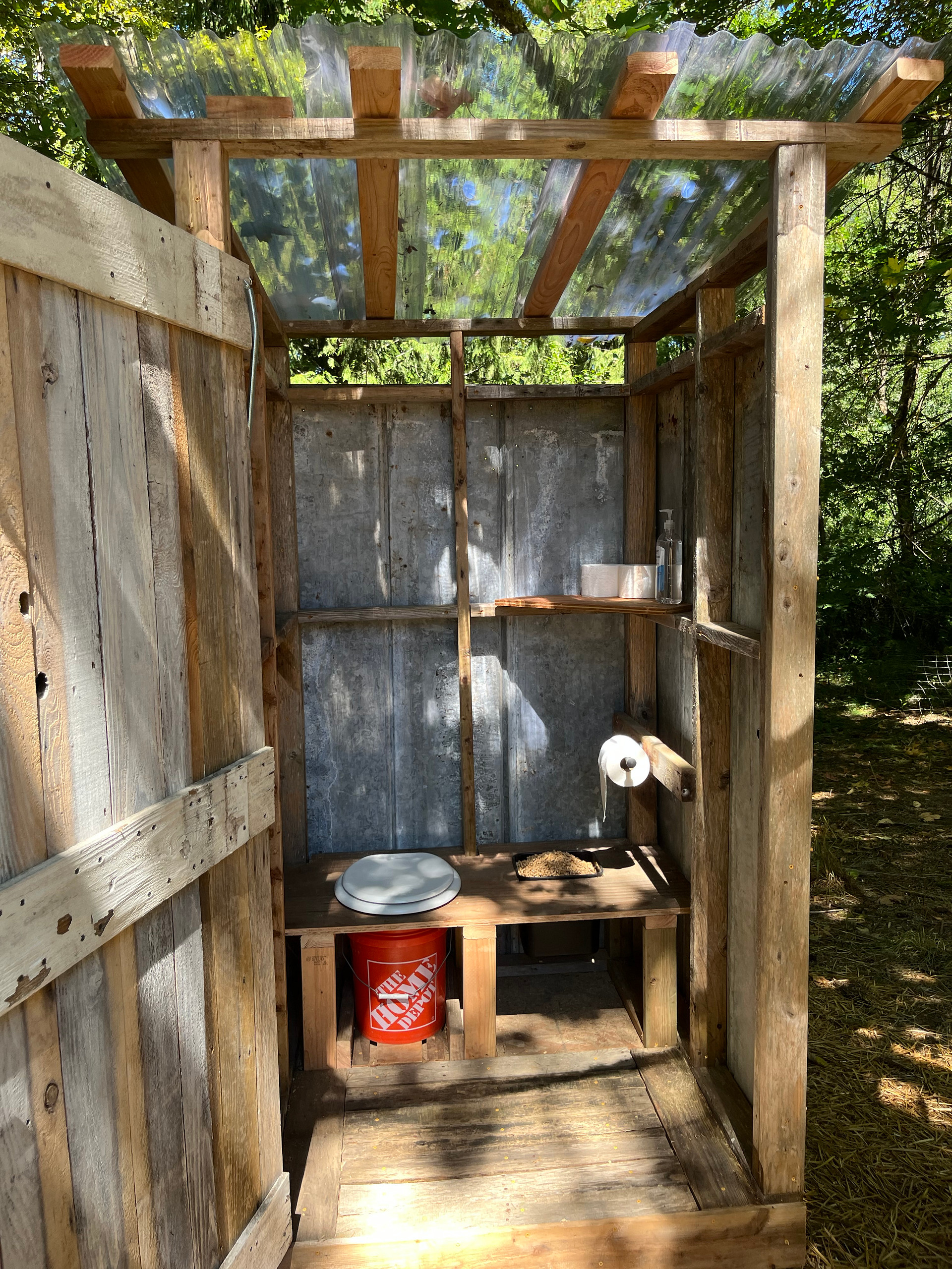 Outhouse features: clear plastic roof for light, inside locking door, composting toilet, wood pellets for smell, toilet paper, and hand sanitizer.
