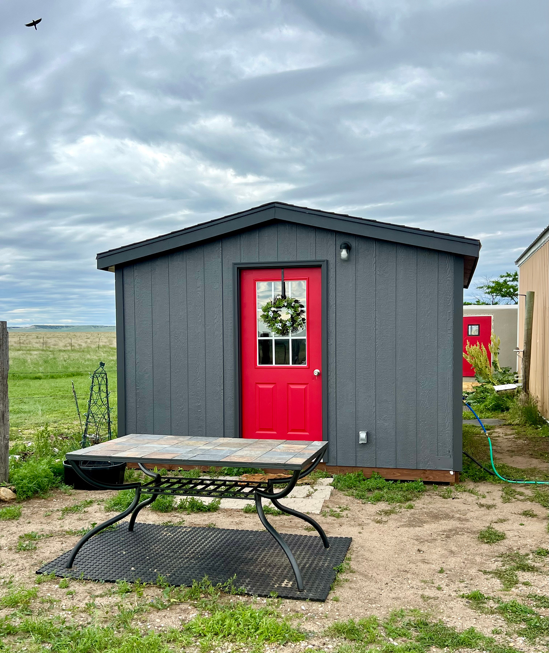 BADLANDS BUNKHOUSE Prairie Retreat, a cozy 12’ x 14’ insulated cabin with a tiny kitchen, stovetop, fridge, sink, basic kitchen supplies, TV, AC and heat. The BADLANDS BATHHOUSE in the background is also part of your private site, and has a compost toilet and hot/cold shower.