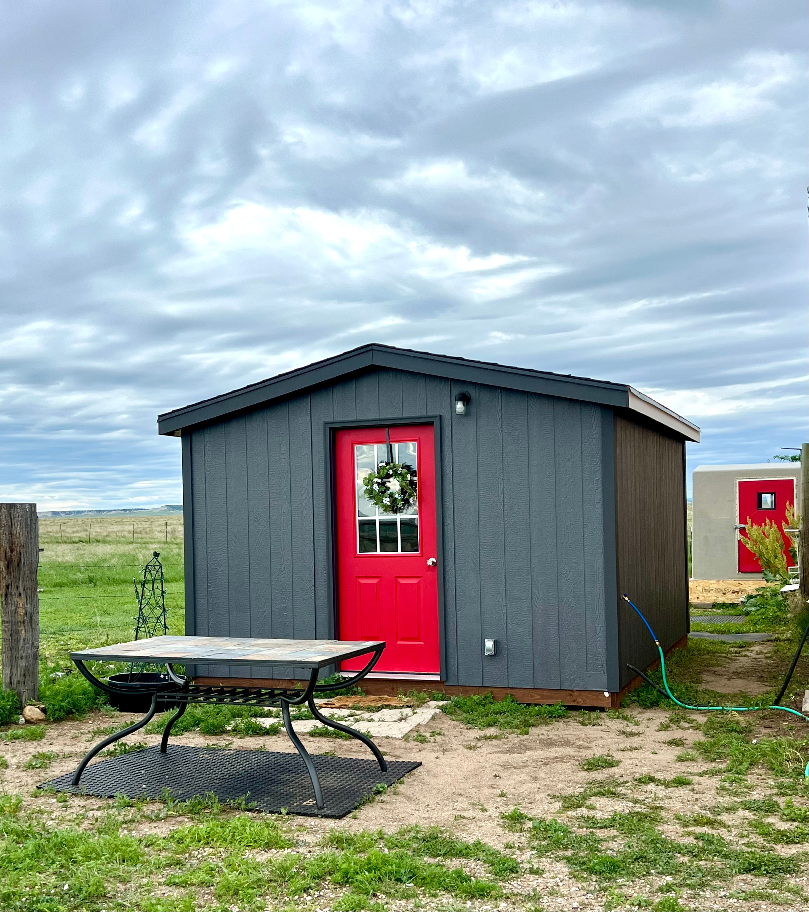 BADLANDS BUNKHOUSE Prairie Retreat, a cozy 12’ x 14’ insulated cabin with a tiny kitchen, stovetop, fridge, sink, basic kitchen supplies, TV, AC and heat. The BADLANDS BATHHOUSE in the background is also part of your private site, and has a compost toilet and hot/cold shower.